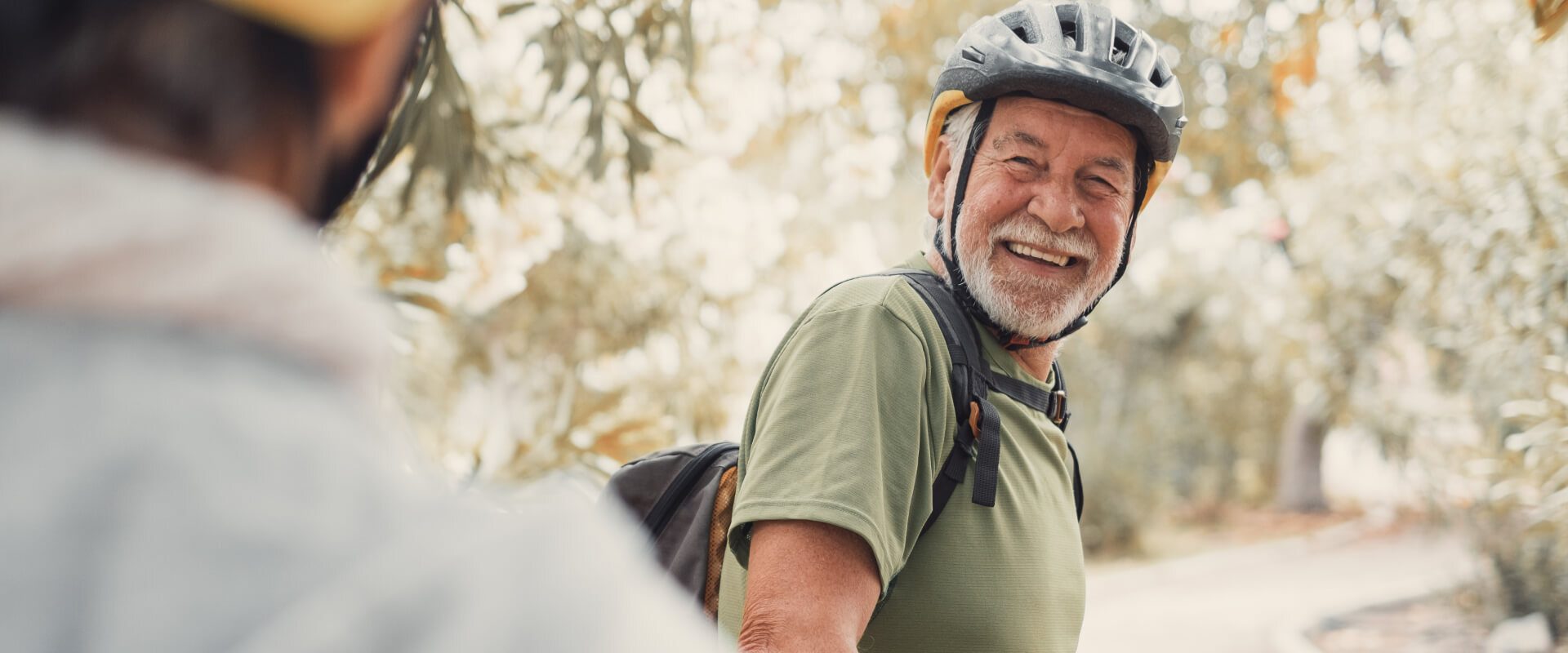 Two happy old mature people enjoying and riding bikes together to be fit and healthy outdoors. Active seniors having fun training in nature. Portrait of one old man smiling in a bike trip with wife